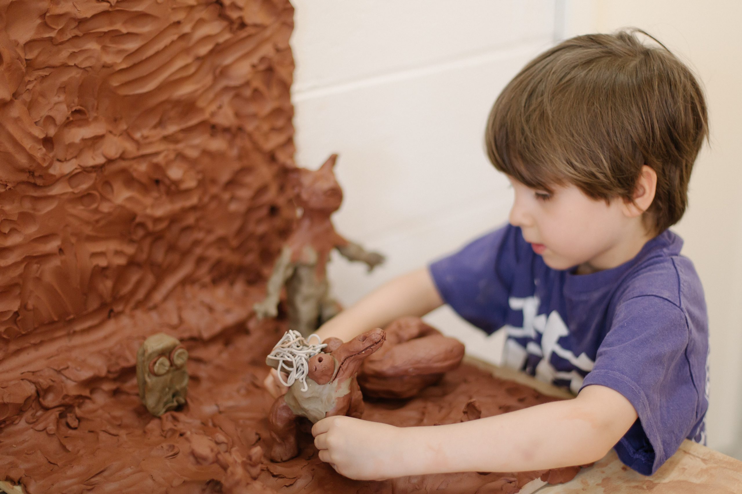 A young child add his clay character to the borwn clay diorama