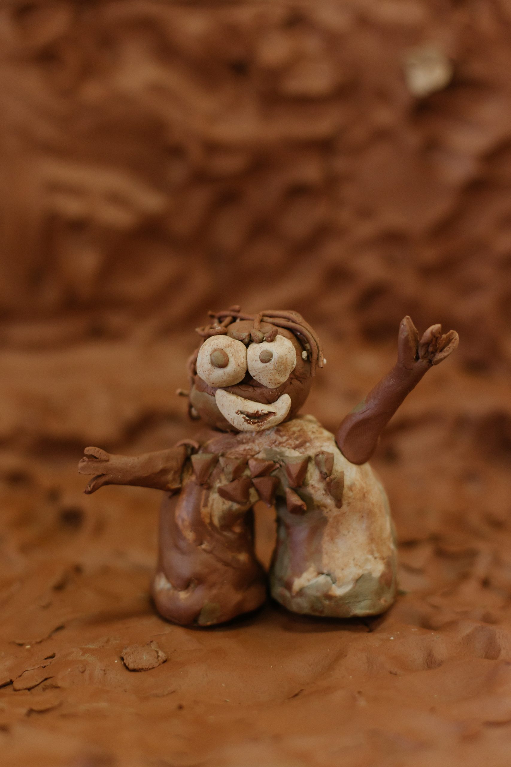A smiling and waving brown clay figurine set in a brown clay diorama.